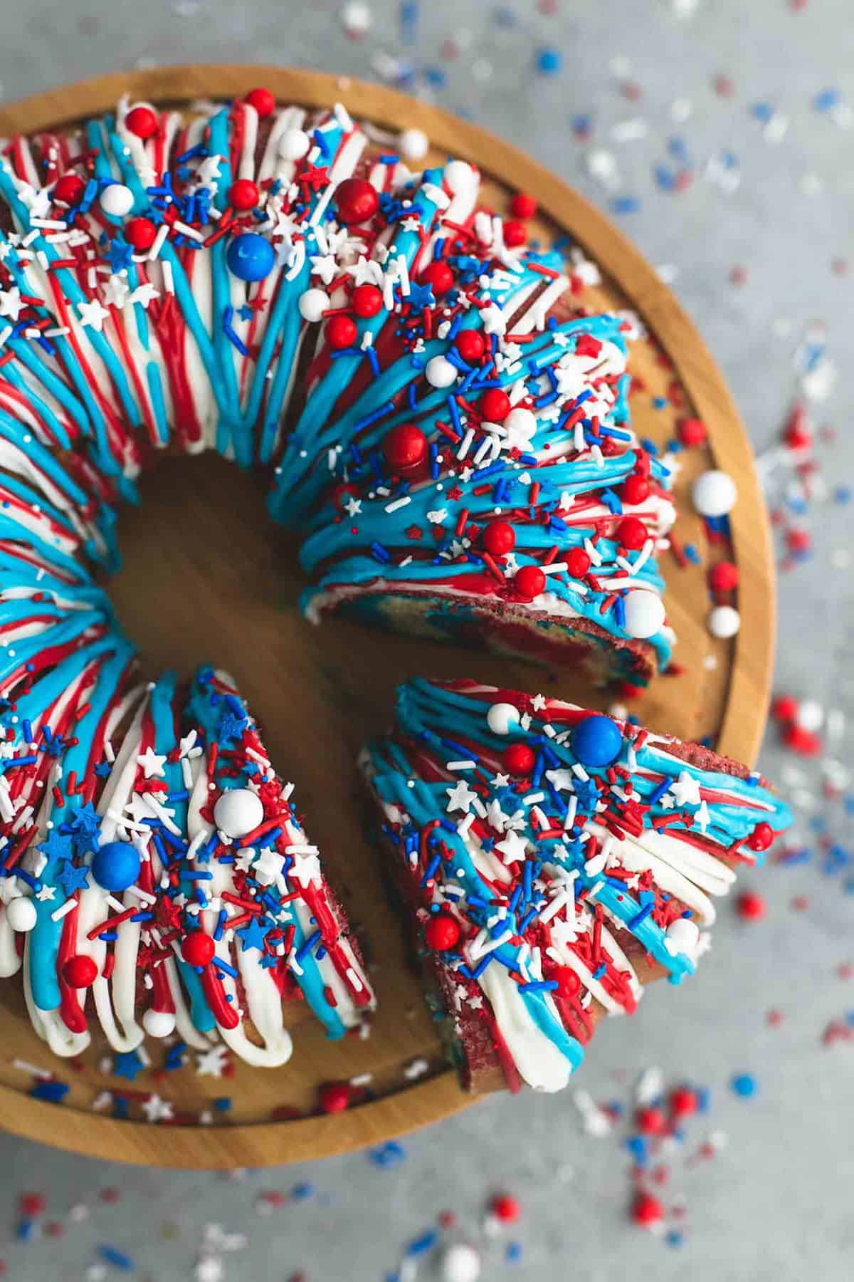 top view of firecracker bundt cake on a cake stand frosted with red, white, and blue frosting and topped with sprinkles with a slice separated from the rest of the cake.