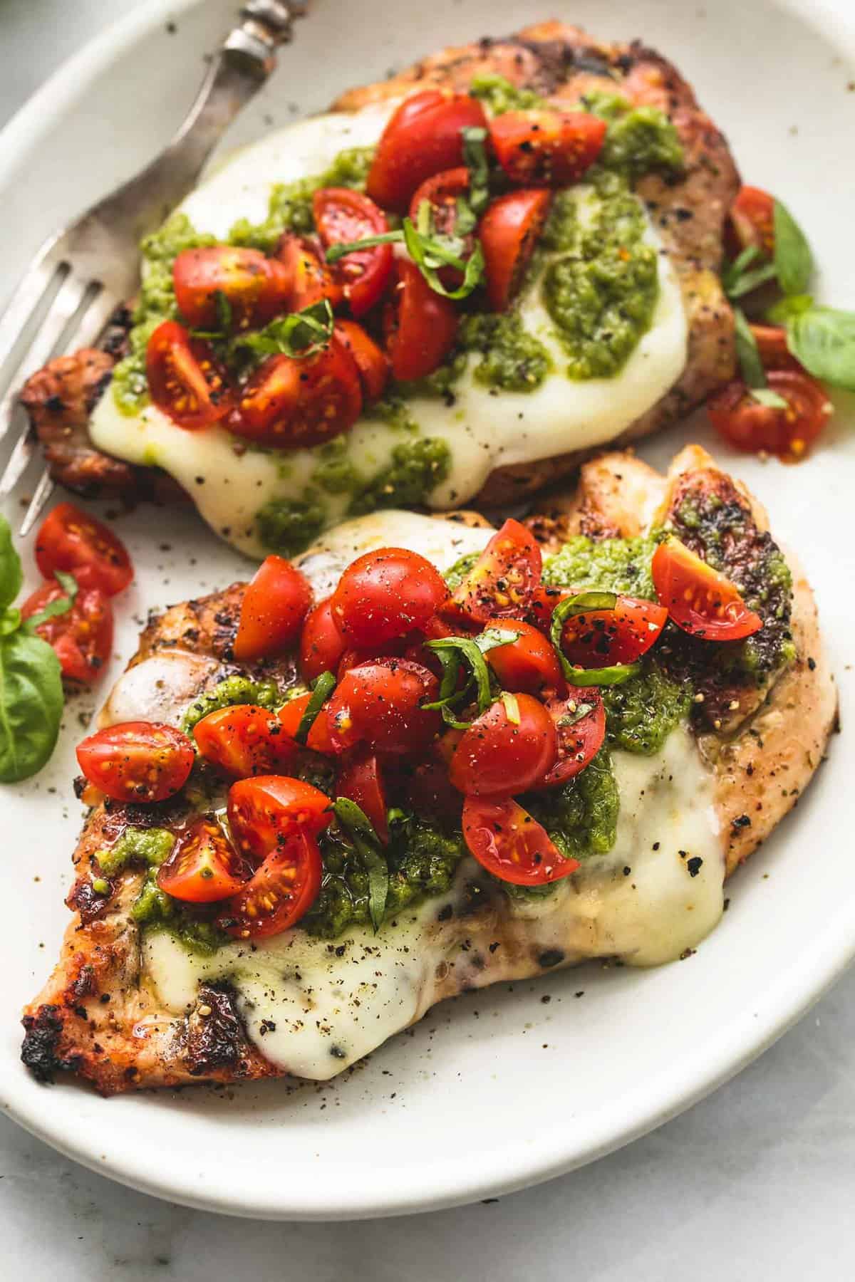 two cooked chicken breasts topped with melted cheese, peso, and tomato bruschetta