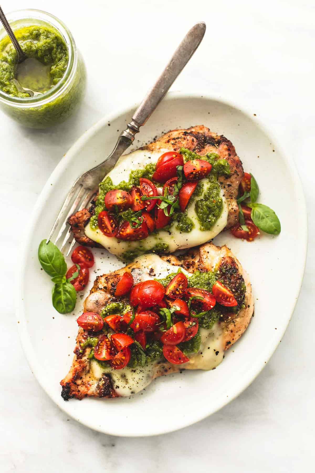overhead view of grilled chicken on plate topped with melted cheese, pesto sauce, and tomatoes