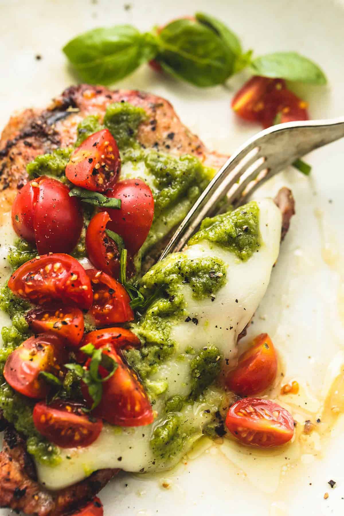 up close view of fork cutting into cooked chicken with cheese, pesto, and tomatoes