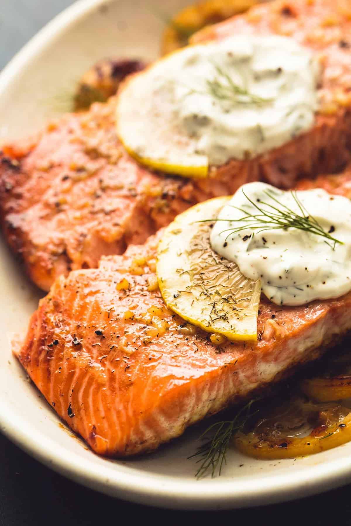 close up of baked salmon with creamy lemon dill sauce on a plate.