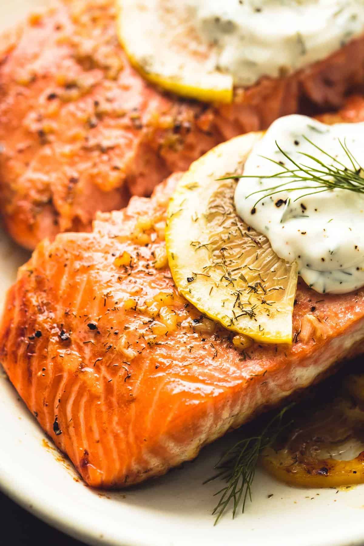 close up of baked salmon with creamy lemon dill sauce on a plate.