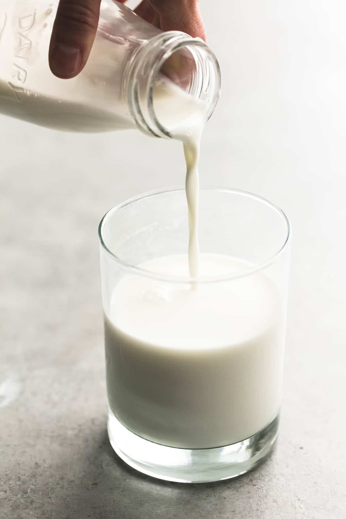 a hand pouring a jar of milk into a glass.