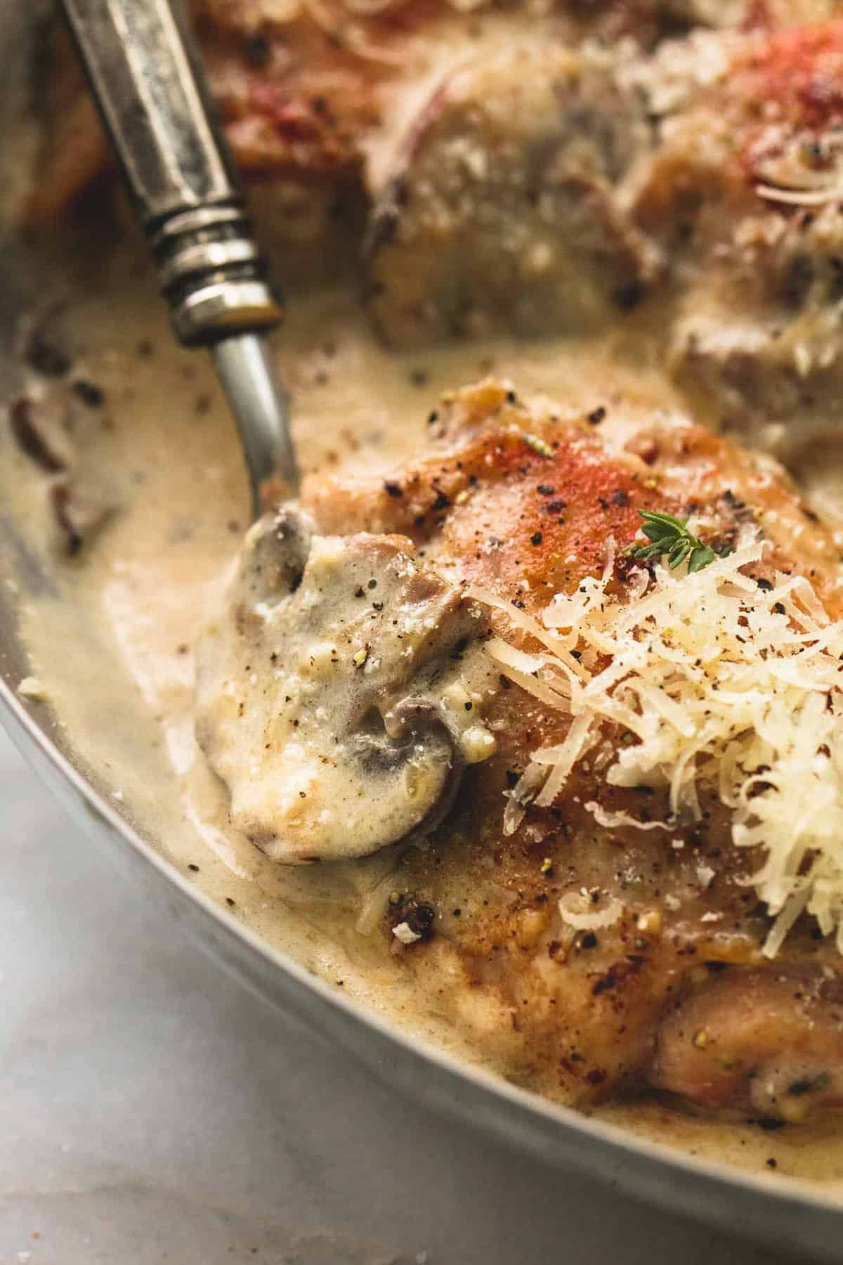 close up of creamy parmesan chicken and mushrooms with a spoon in a pan.