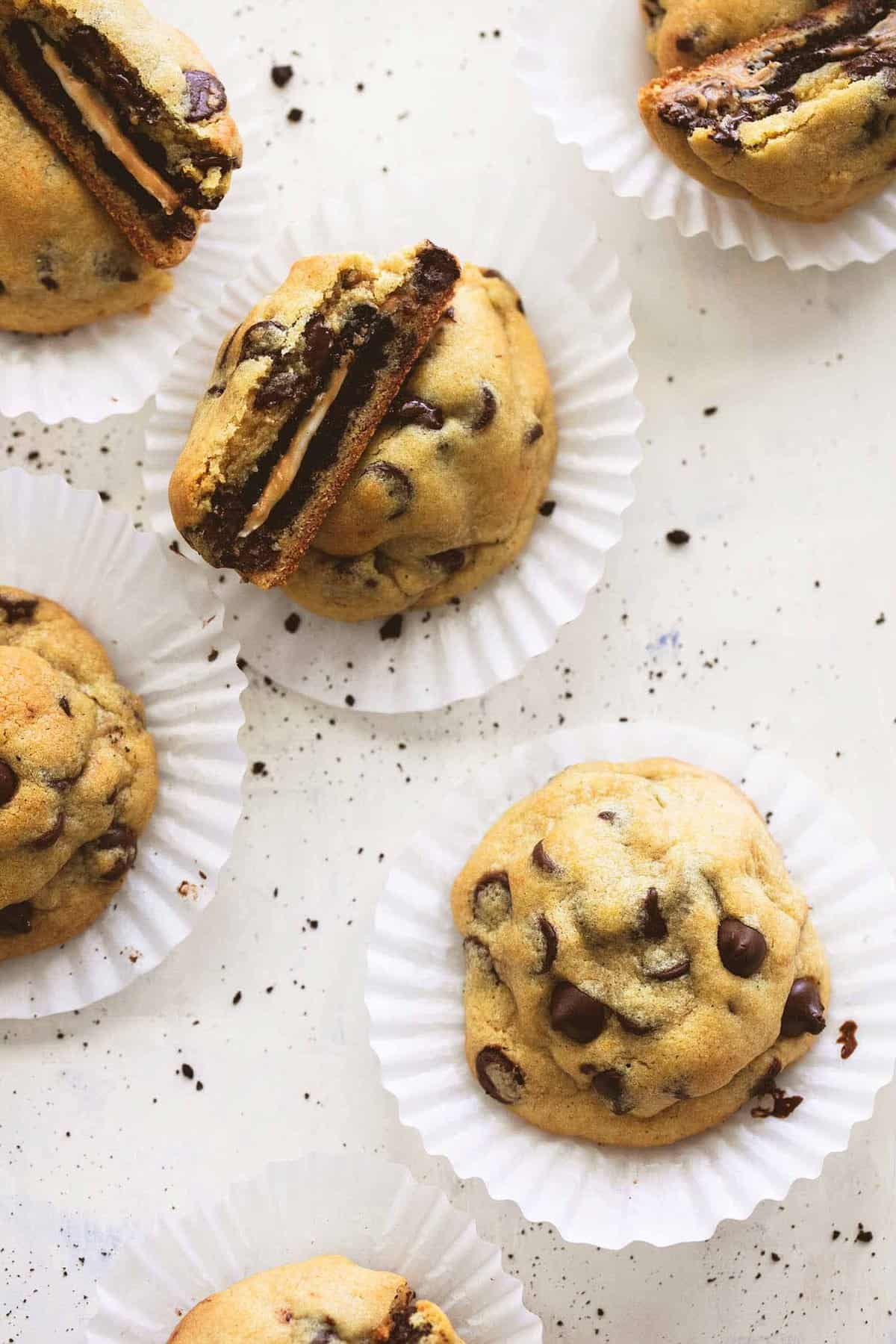 close up top view of peanut butter Oreo stuffed chocolate chip cookies on cupcake liners with a couple cookies broken in half to show the middle.