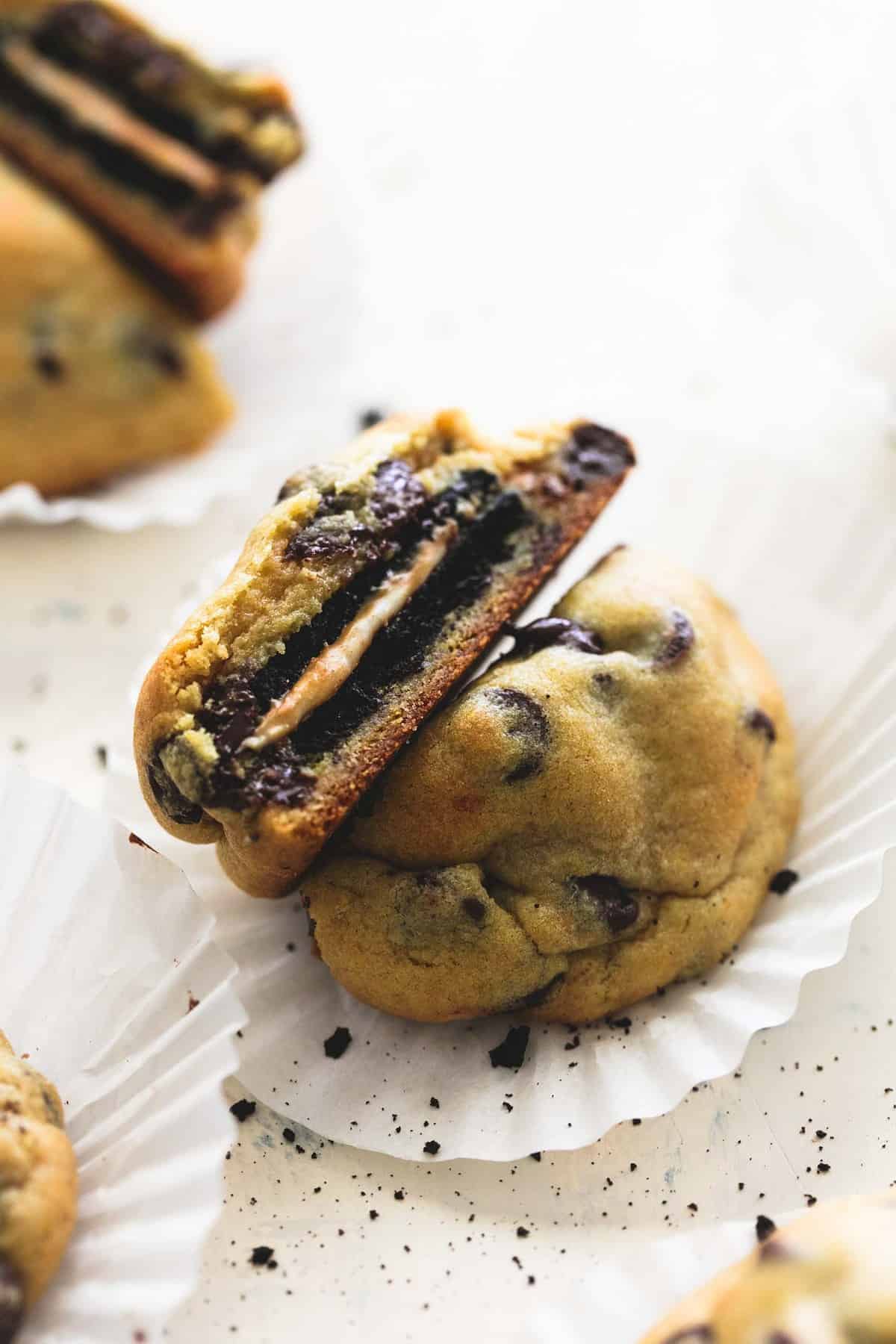 a peanut butter Oreo stuffed chocolate chip cookie on a cupcake liner broken in half to show the middle with another cookie also broken in half in the background.