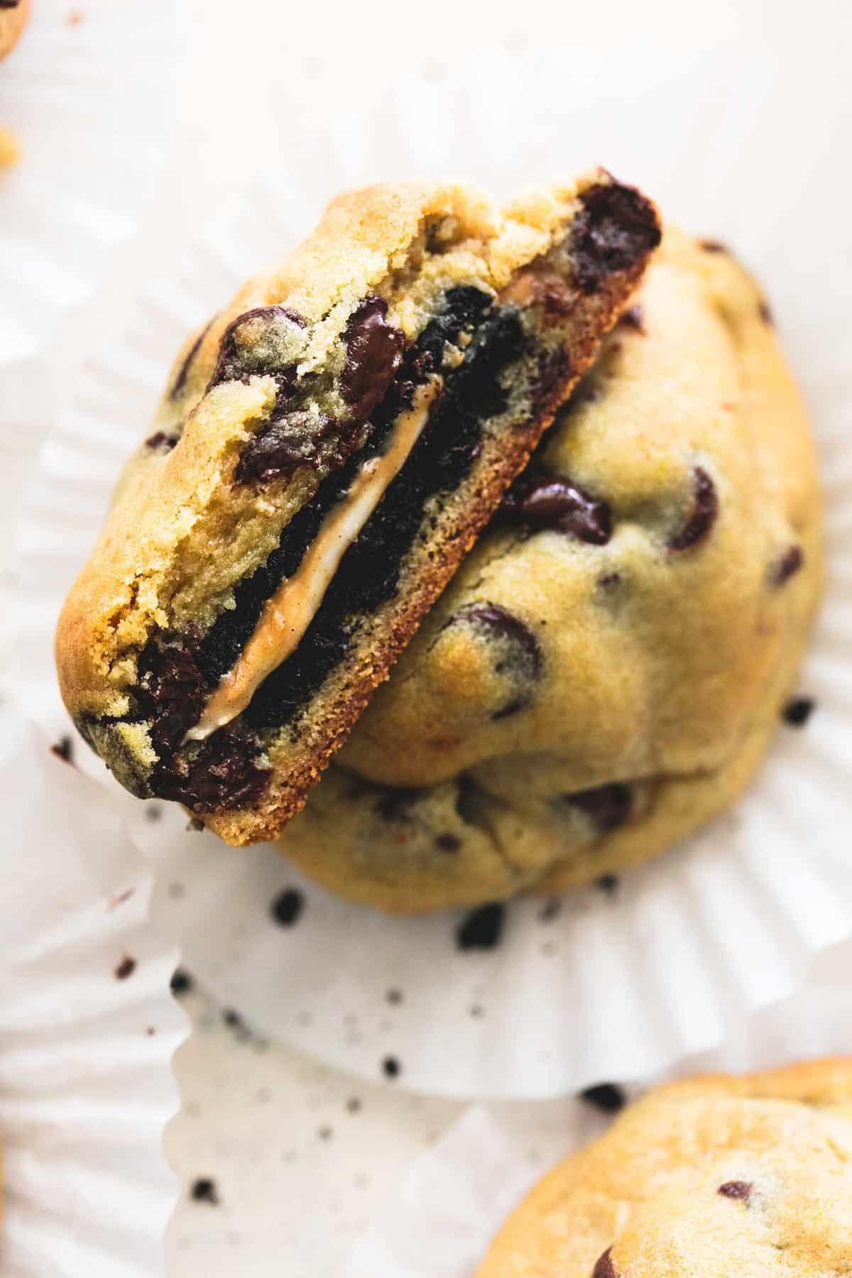 a peanut butter and Oreo stuffed chocolate chip cookie on a cupcake liner broken in half with one half leaning on the other fadein upward.