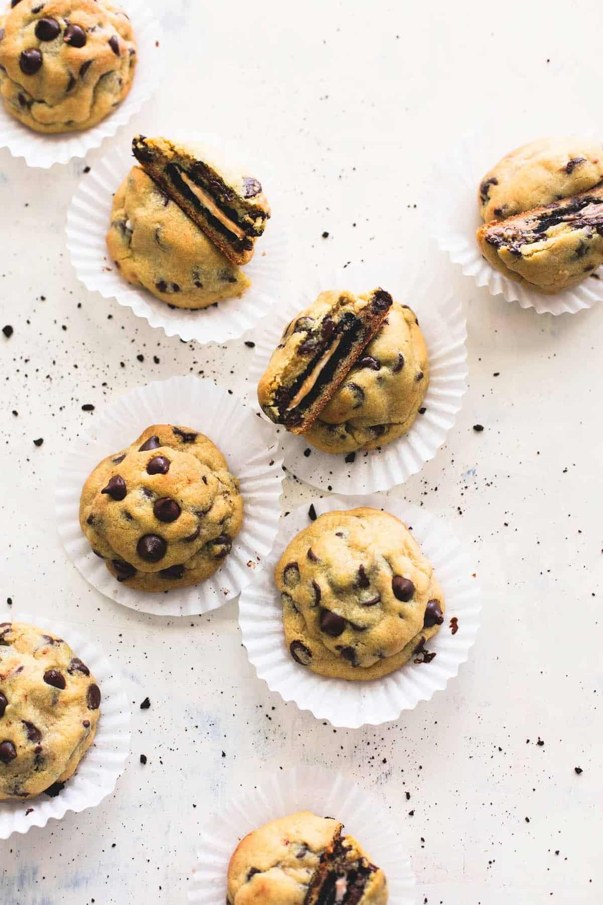 top view of peanut butter Oreo stuffed chocolate chip cookies with a couple broken in half and laying on top of each other all on cupcake liners.