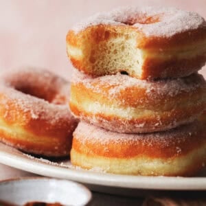 Close up of a stack of fried yeast donuts with the top donut missing a bite.
