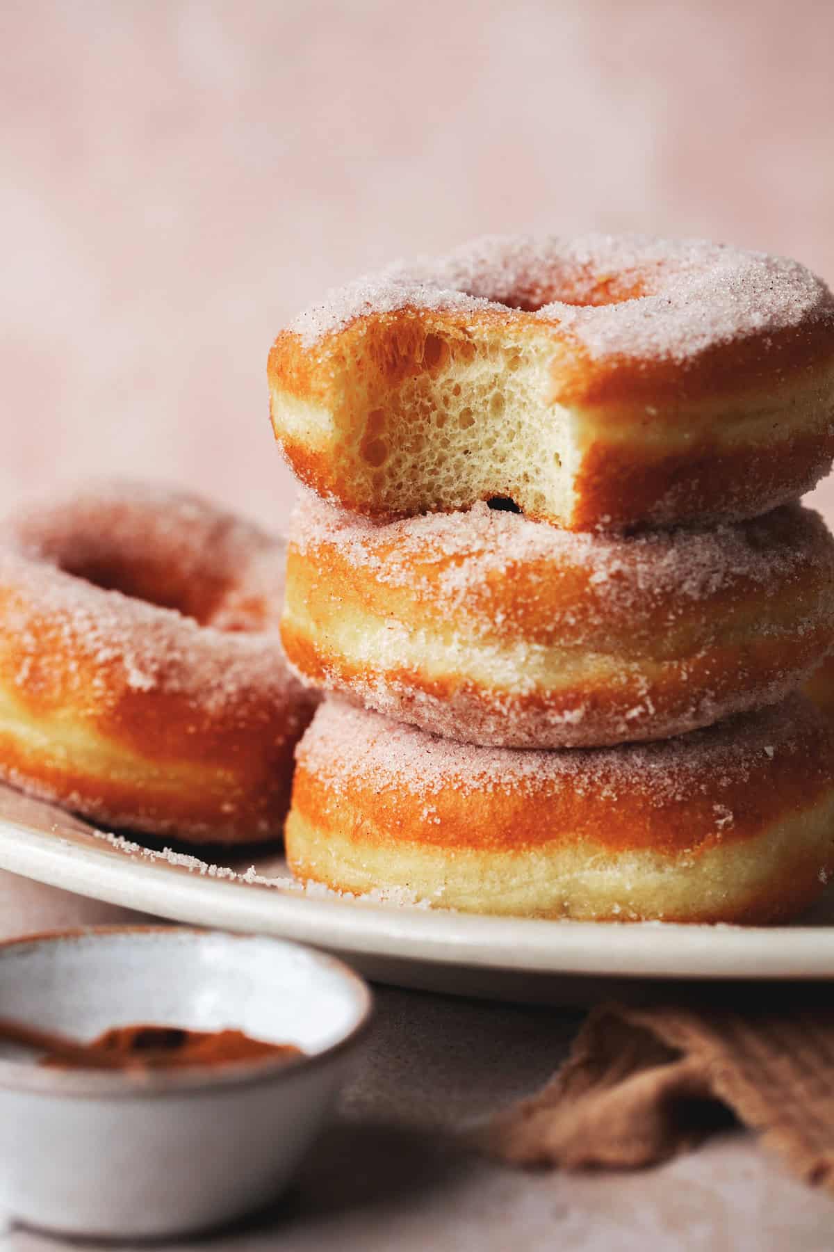Close up of a stack of fried yeast donuts with the top donut missing a bite.