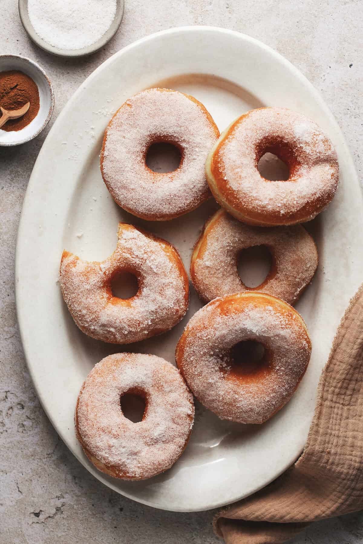 Overhead overhead a white pate with fried yeast donuts with one with a bite taken out. 