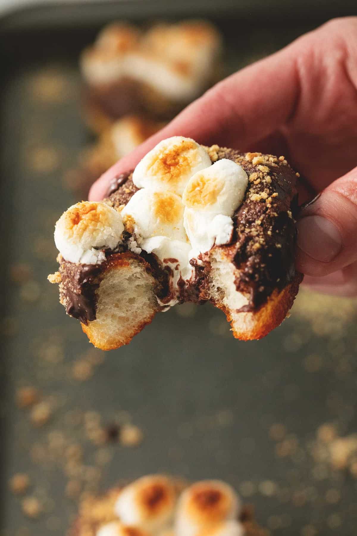 a hand holding up a s'mores donuts with a bite missing.