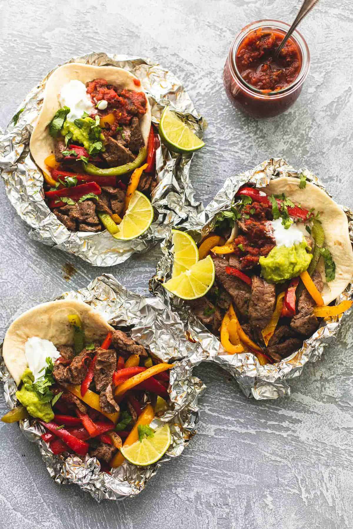 top view of steak fajita foil packs with a jar of salsa on the side.