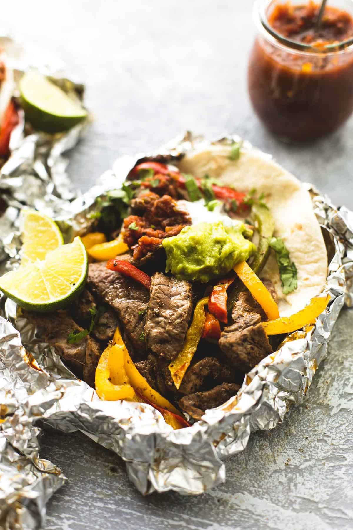 a steak fajita foil pack with salsa in a jar in the background.