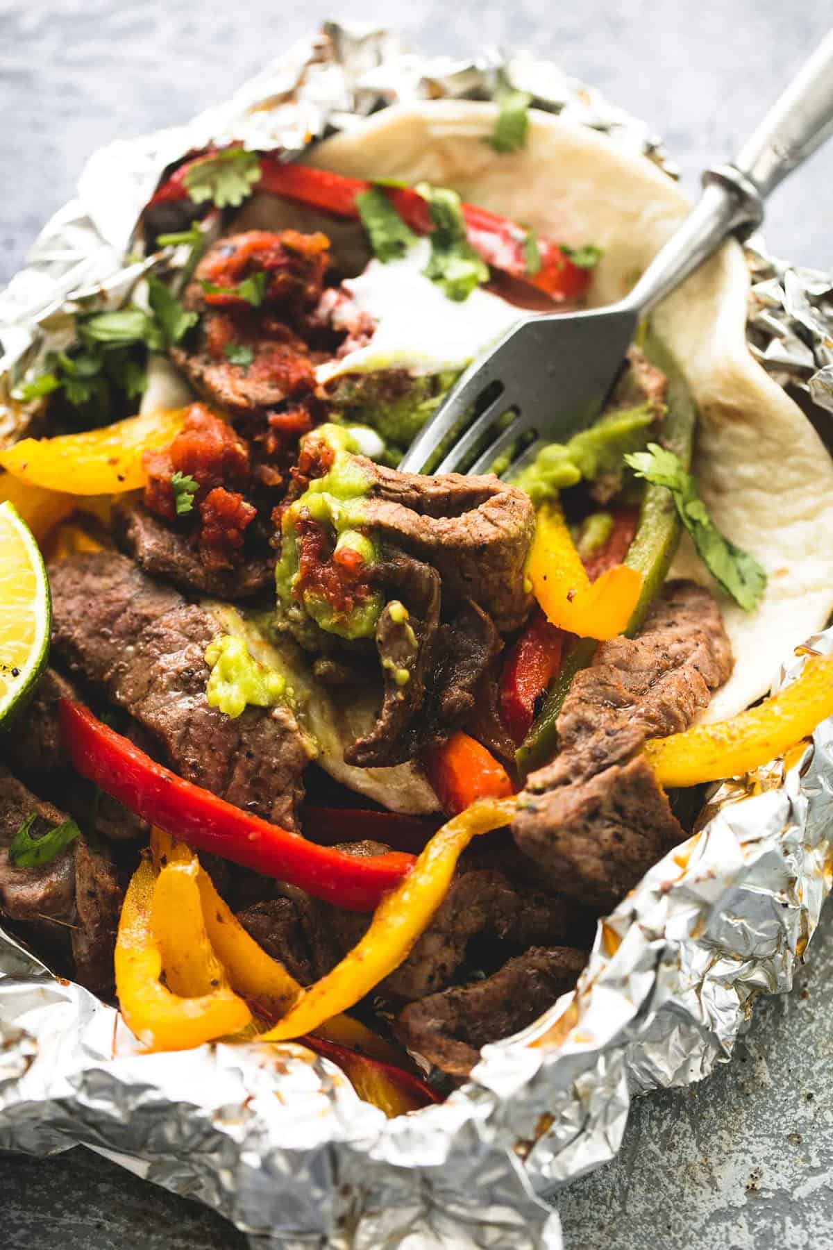 close up of a steak fajita foil pack with a fork.