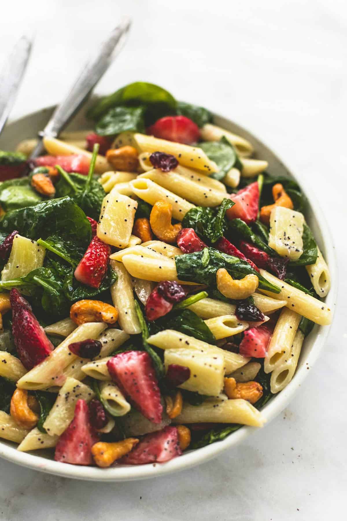 strawberry spinach pasta salad with orange poppy seed dressing with a fork on a plate.