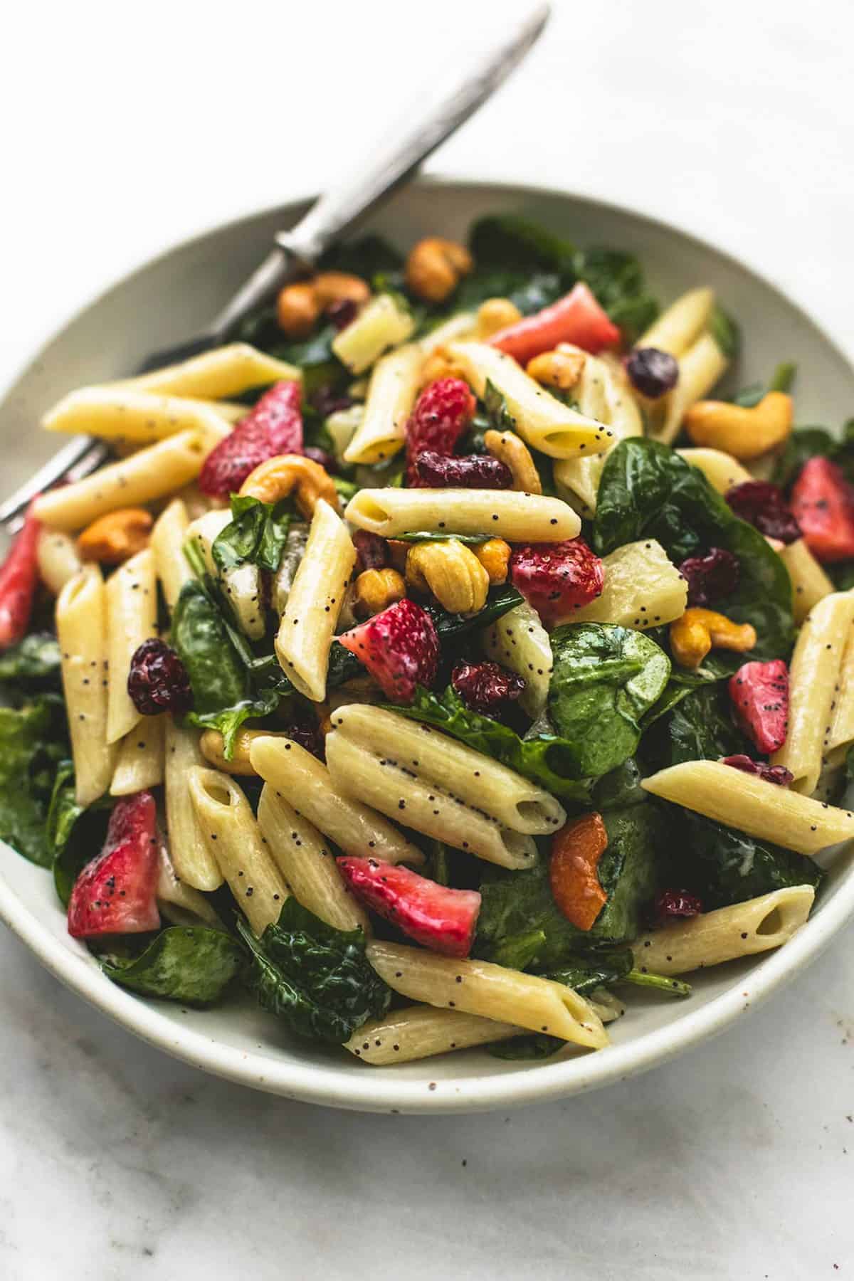 strawberry spinach pasta salad with orange poppy seed dressing with a fork on a plate.