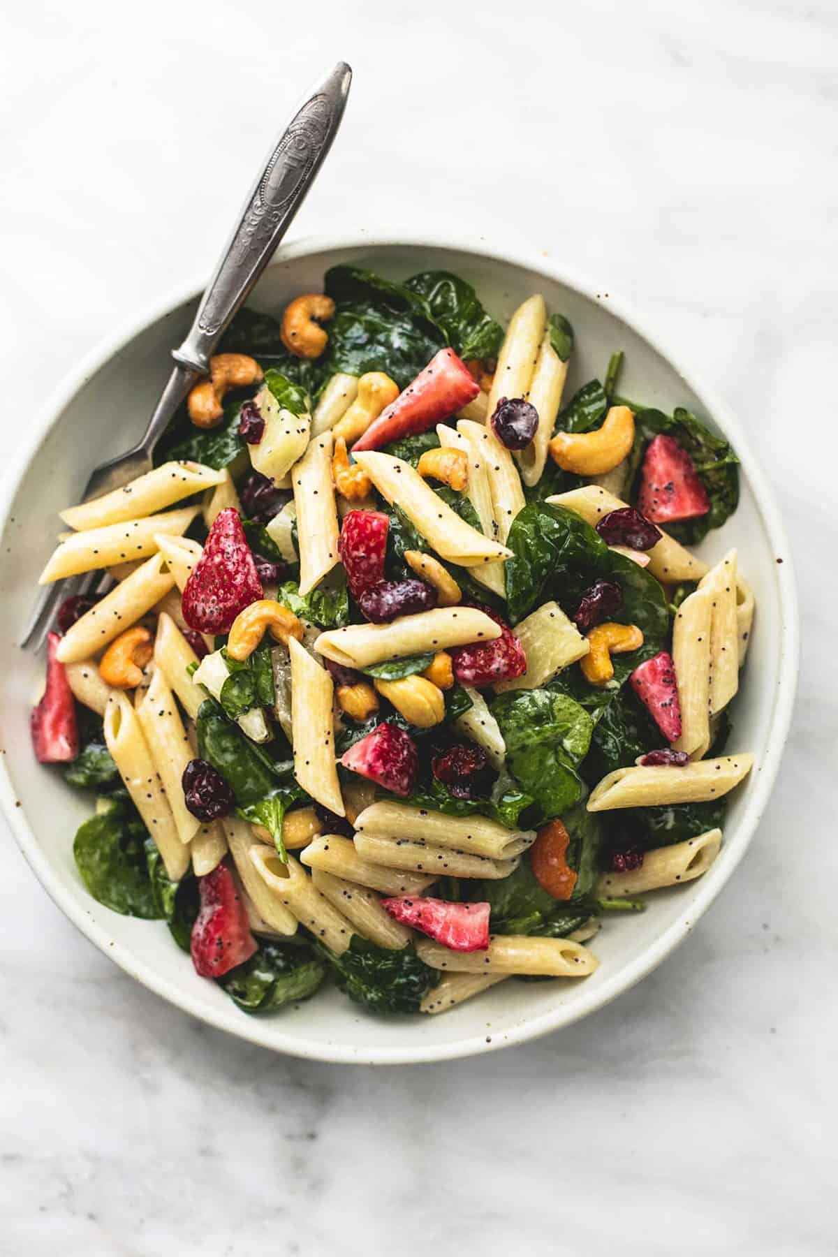 top view of strawberry spinach pasta salad with orange poppy seed dressing with a fork on a plate.