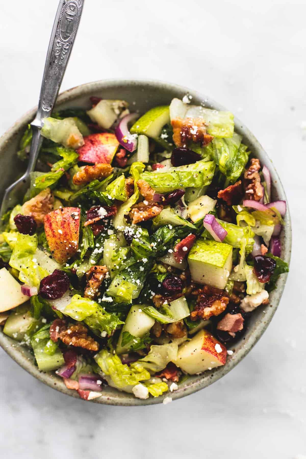 top view of chopped Autumn salad with apple cider dressing with a fork in a bowl.