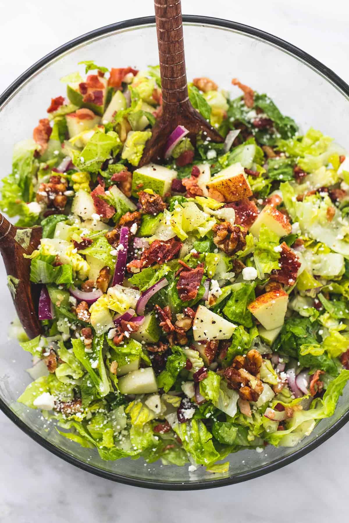 top view of chopped Autumn salad with apple cider dressing with a wooden spoon in a glass bowl.