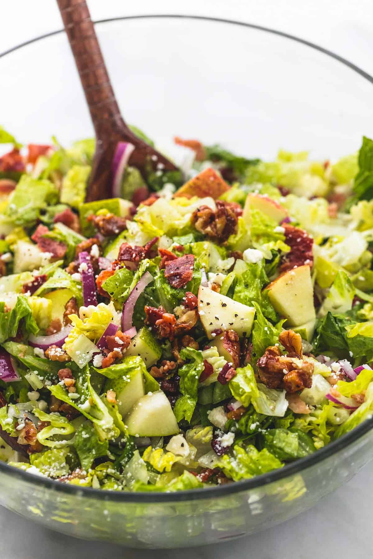 close up of chopped Autumn salad with apple cider dressing with a wooden spoon in a glass bowl.