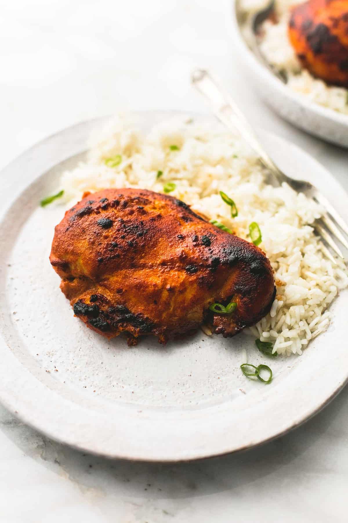 a piece of baked tandoori chicken with rice and a fork on a plate.
