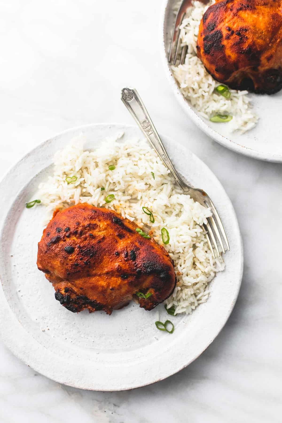 top view of a piece of baked tandoori chicken with rice and a fork on a plate.