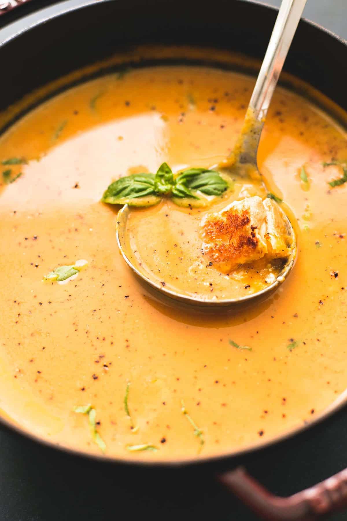 close up of creamy pumpkin soup with grilled cheese croutons with a serving spoon in a pan.