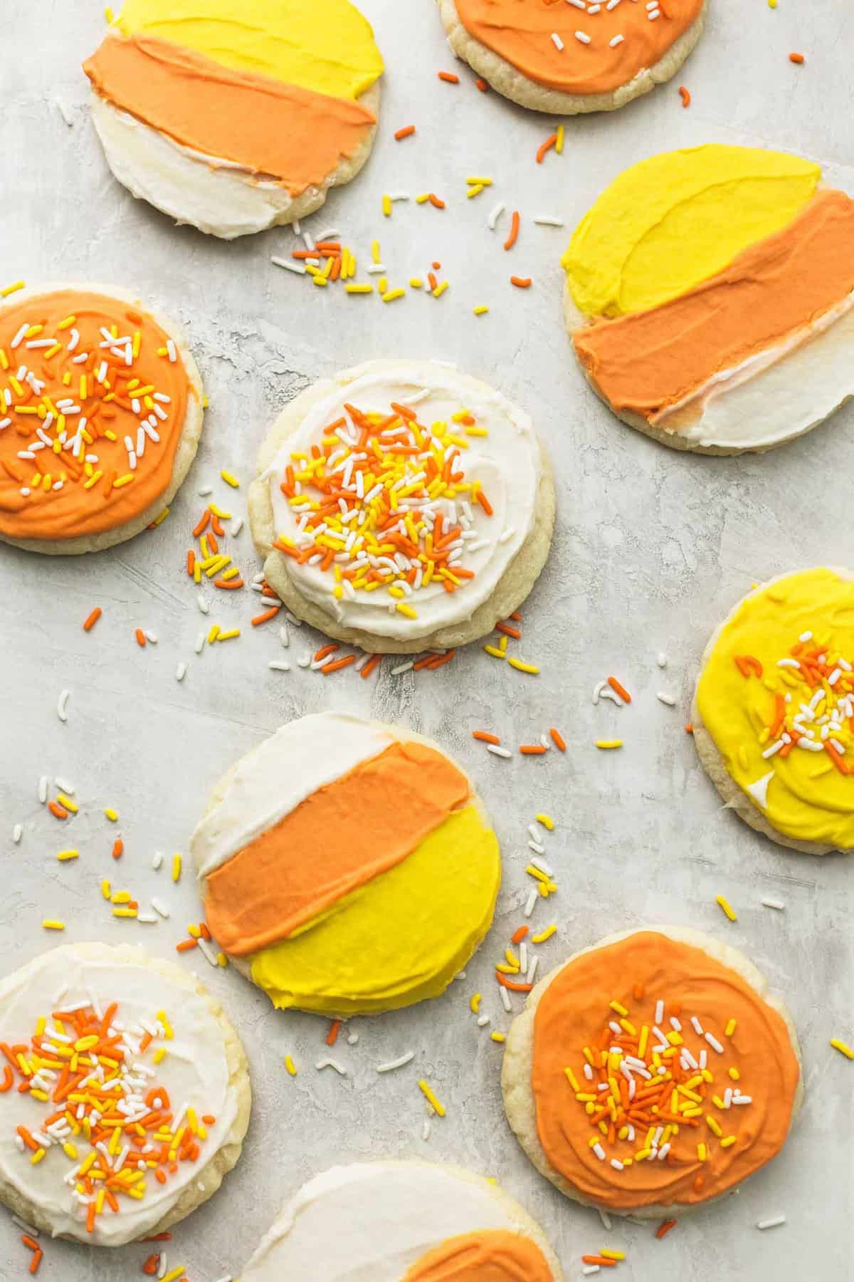 top view of candy corn sugar cookies some frosted like candy corn and others frosted with a single color of orange, white, and yellow with sprinkles on top.