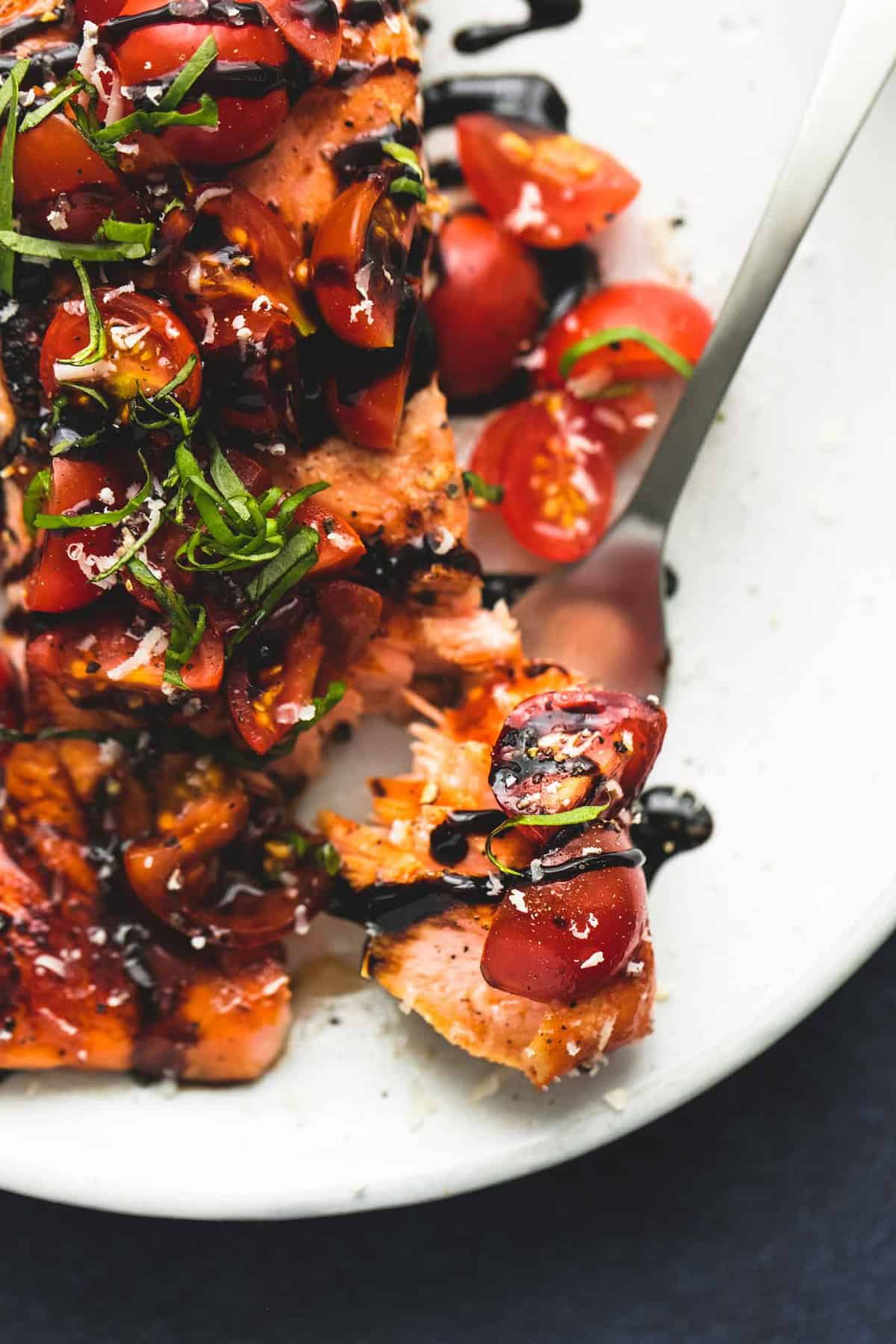 close up of a bite of honey balsamic bruschetta salmon on a fork next to the rest of the salmon on a plate.