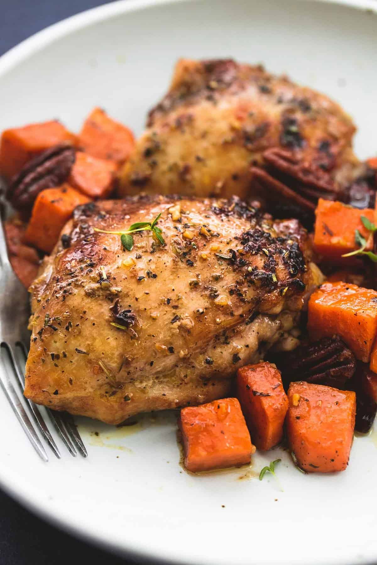 close up of honey roasted chicken and sweet potatoes skillet with a fork on a plate.