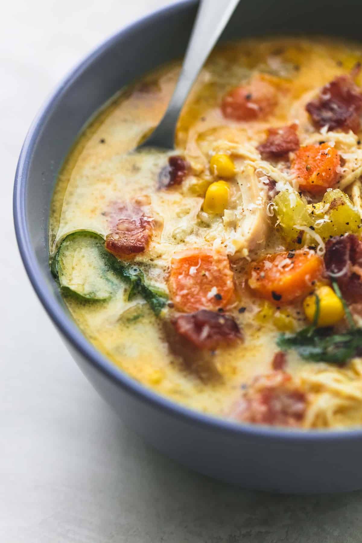 close up of slow cooker New England chicken chowder with a spoon in a bowl.