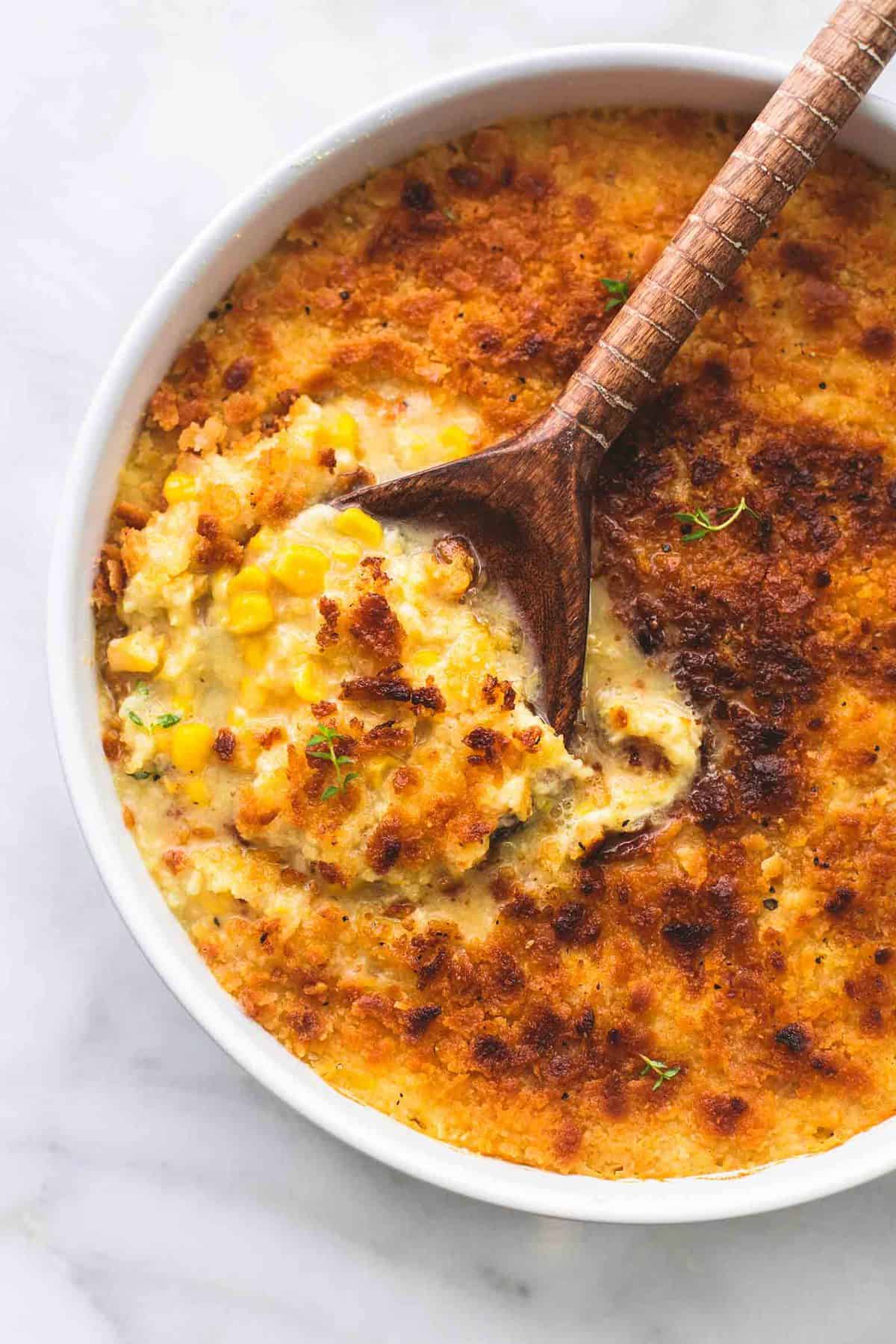 top view of baked parmesan creamed corn with a serving spoon in a round serving tray.