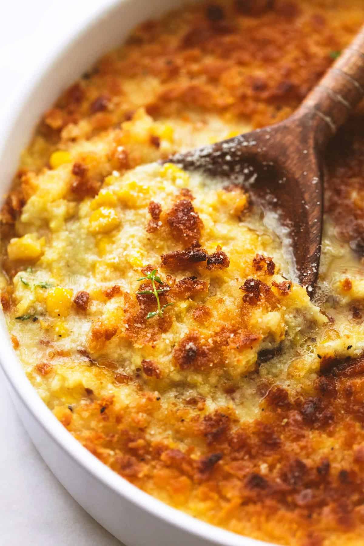 close up of baked parmesan creamed corn with a serving spoon in a round tray.