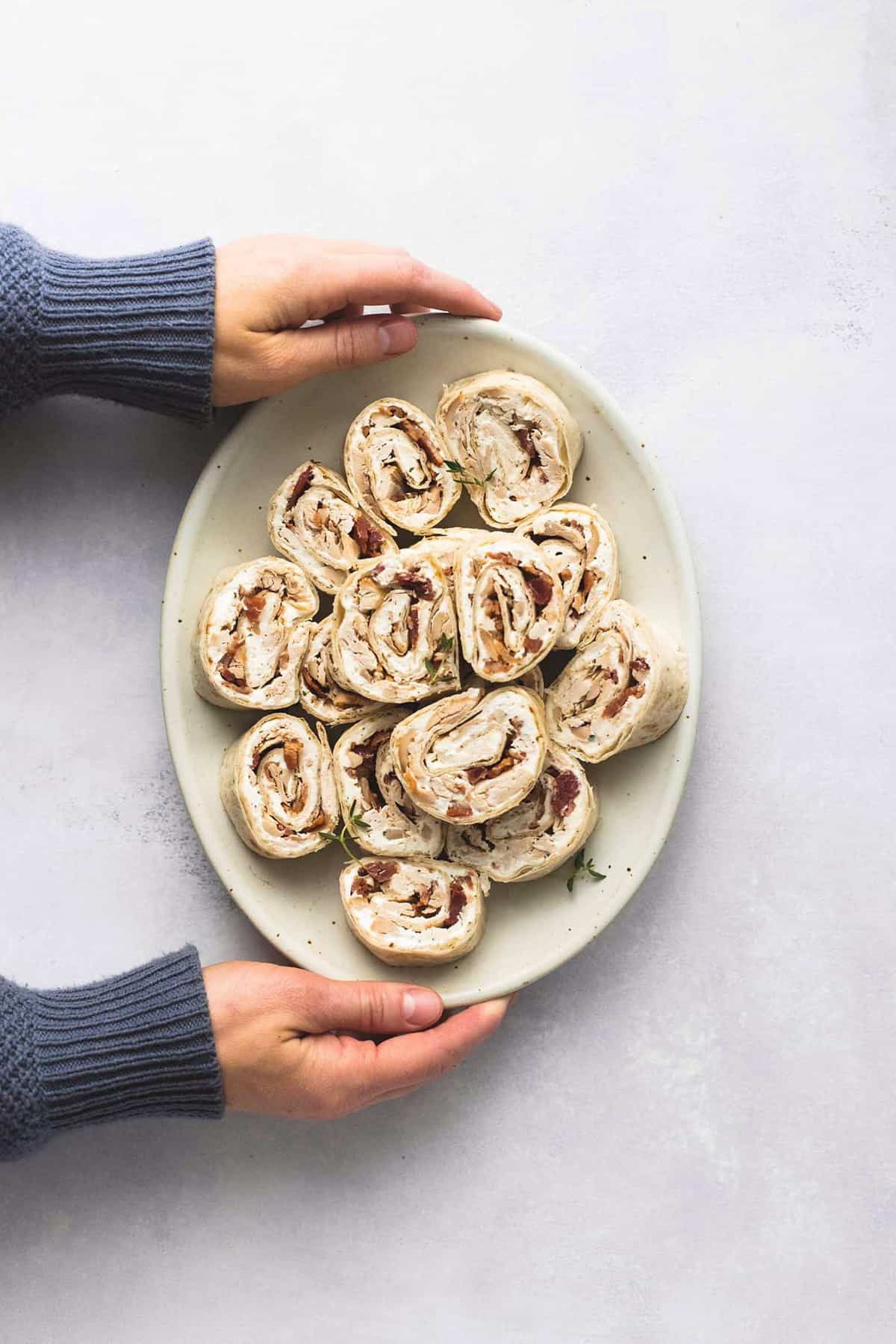 top view of hands holding a plate of chicken bacon ranch pinwheels.