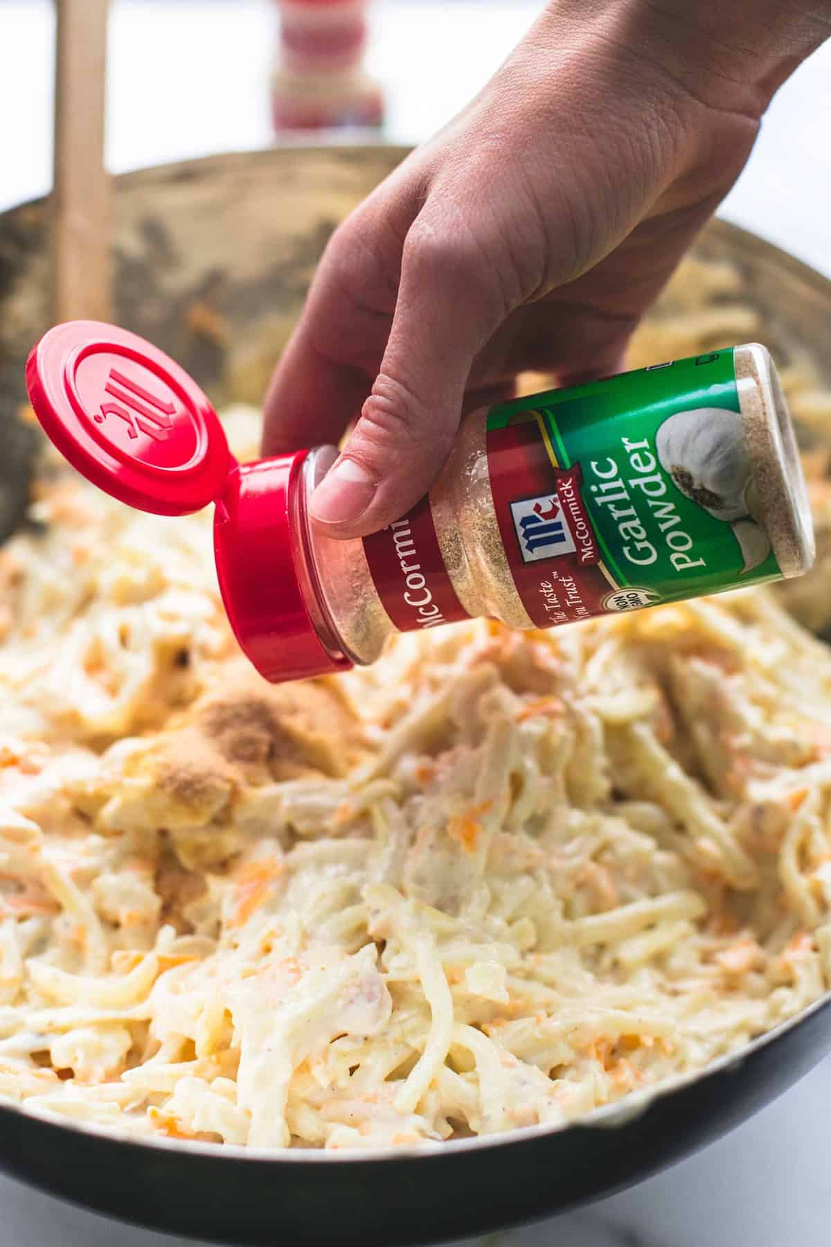 a hand pouring garlic powder into a pan of company potatoes.