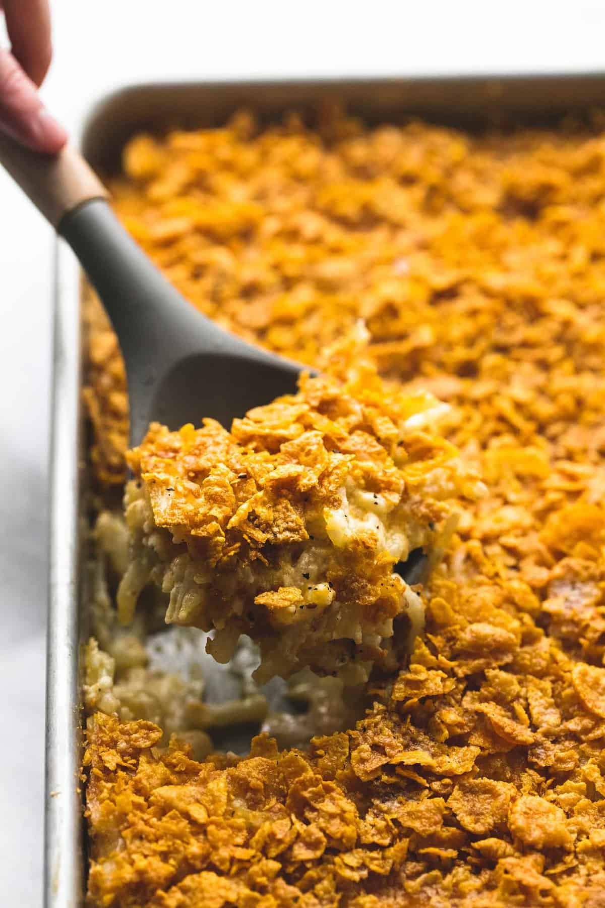 a serving spoon scooping some company potatoes out of a baking sheet.