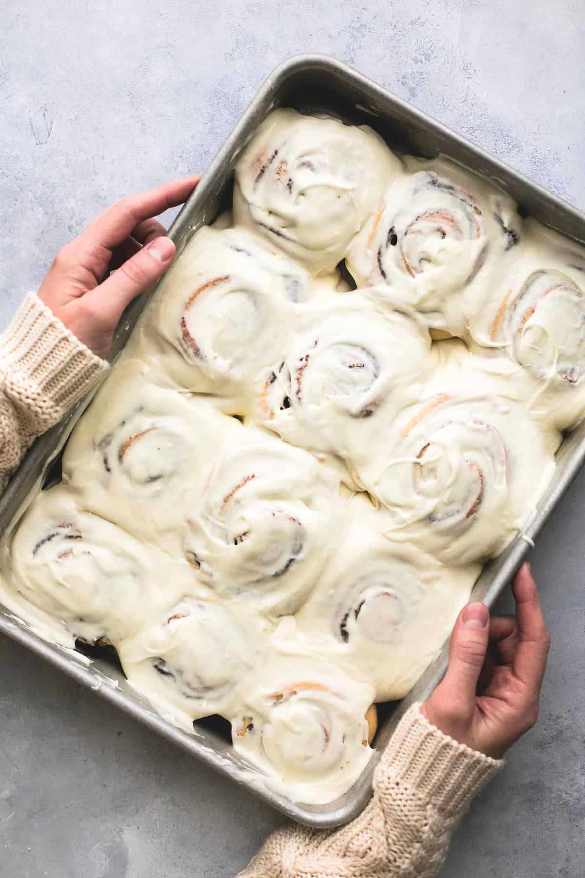 top view of hands holding a baking sheet of eggnog cinnamon rolls.