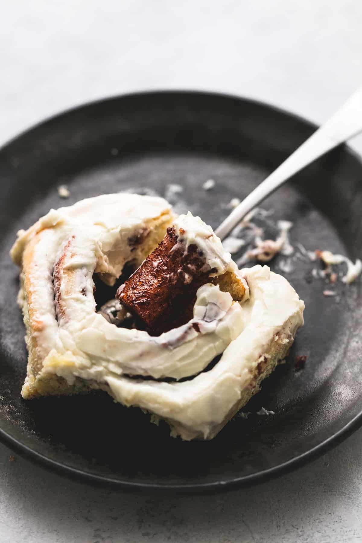 a eggnog cinnamon roll with the middle sitting on a fork underneath the roll on a plate.