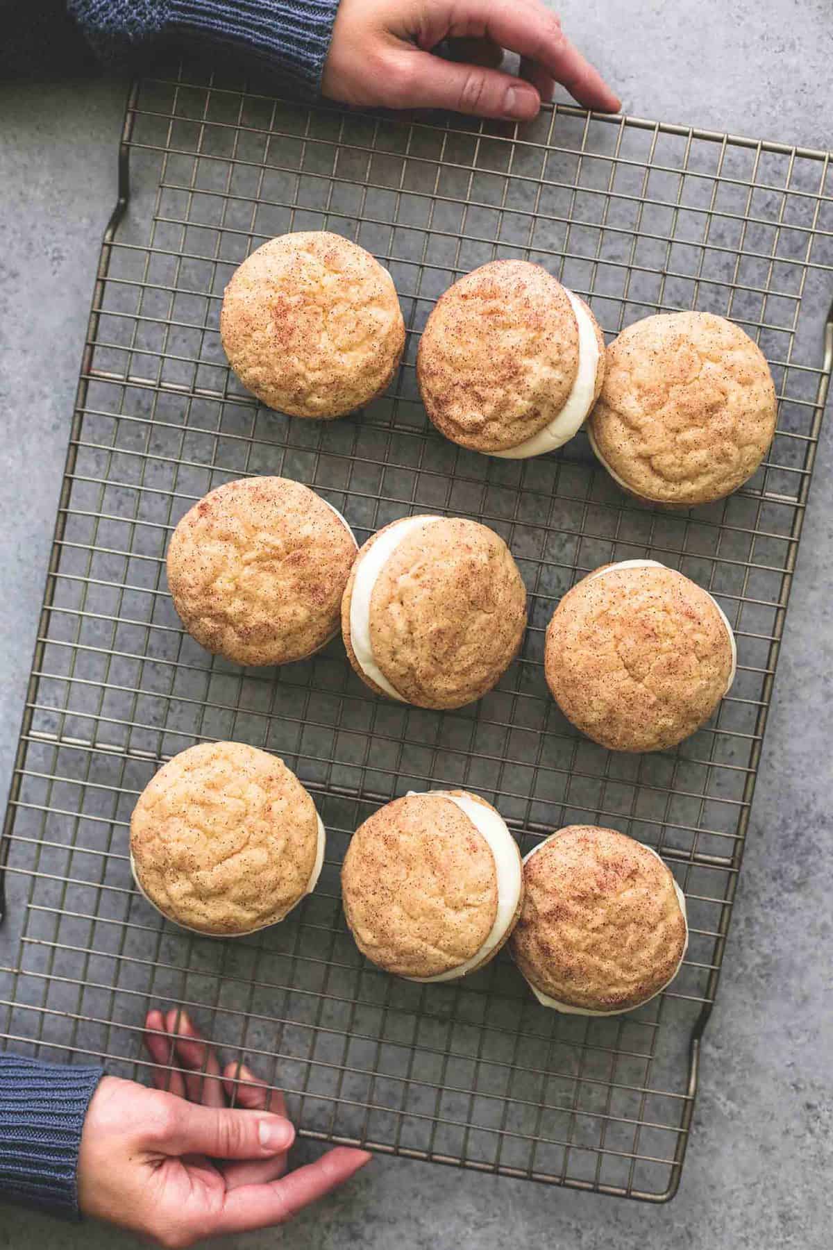 top view of hands holding a cooling rack with eggnog snickerdoodle whoopie pies on it.