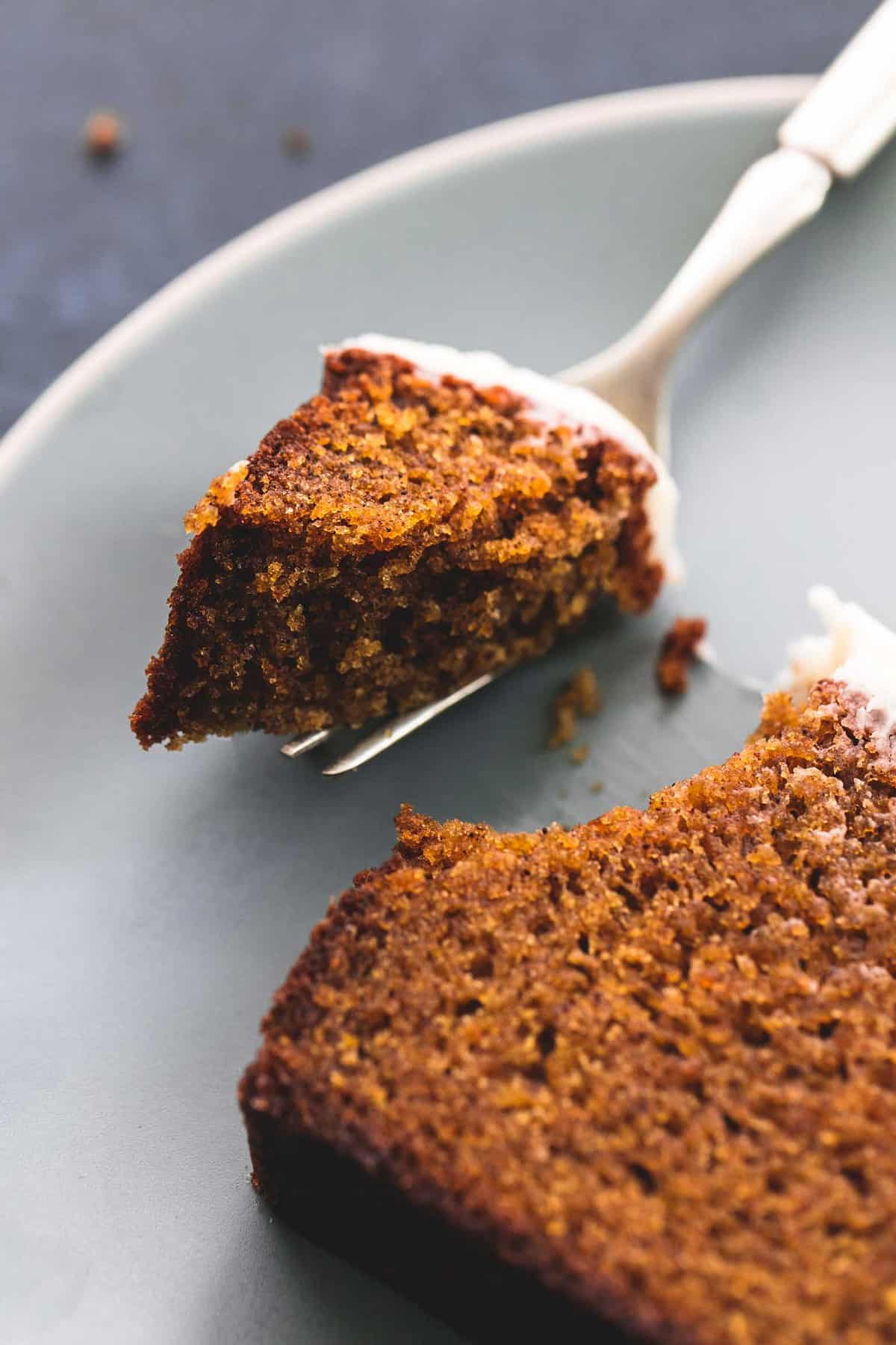 close up of a bite of cream cheese frosted pumpkin bread on a fork next to the rest of the slice on a plate.