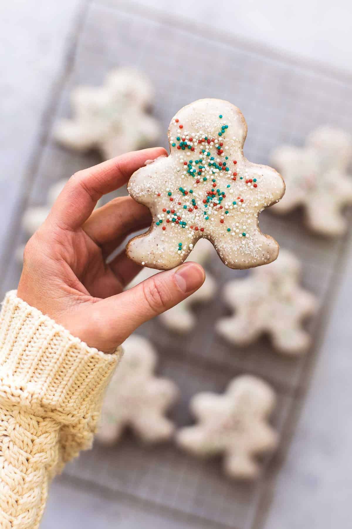 a hand holding a gingerbread sugar cookie above a cooling rack of more cookies.