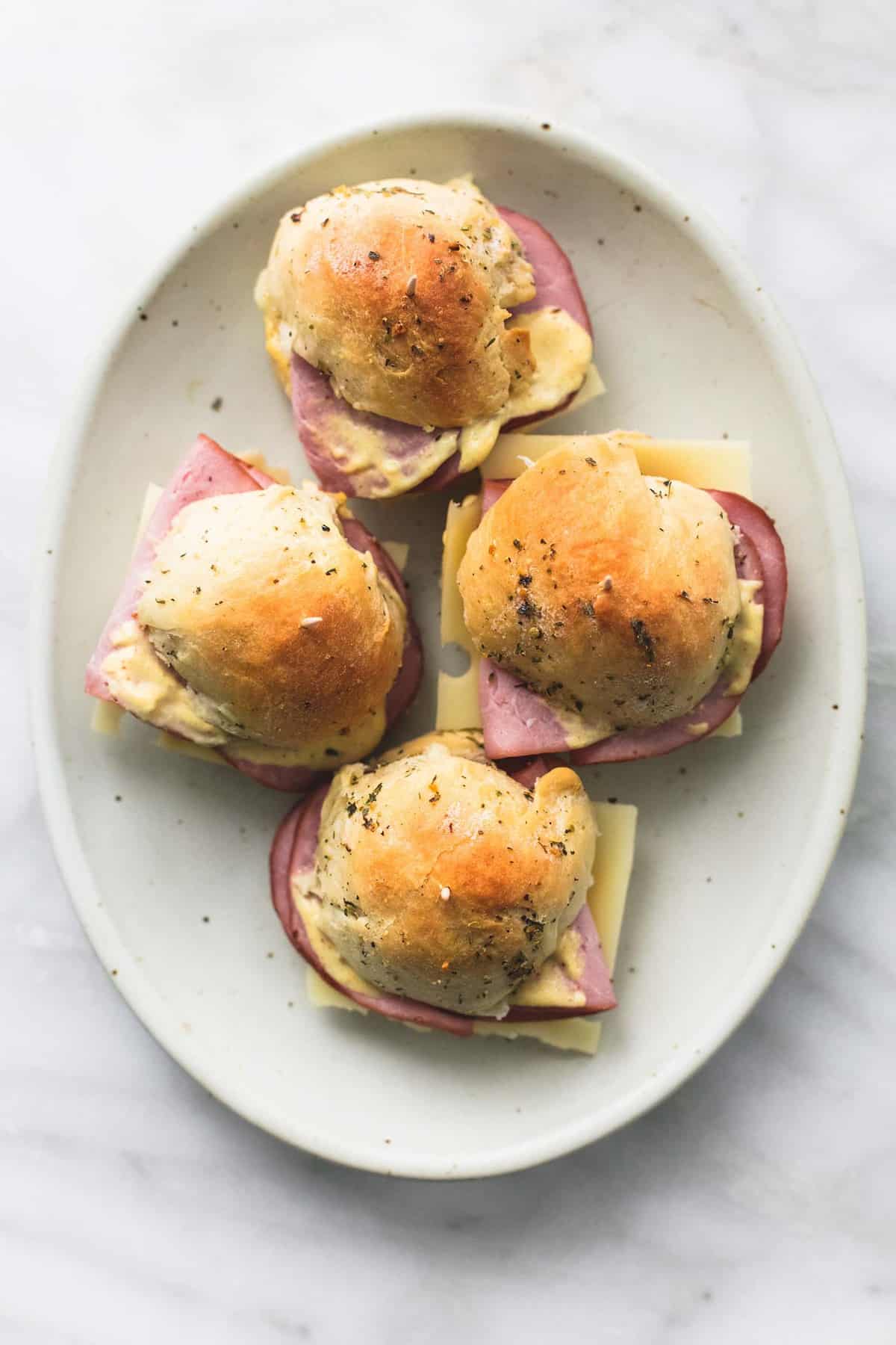 top view of ham and cheese sliders on buttery herb rolls on a plate.