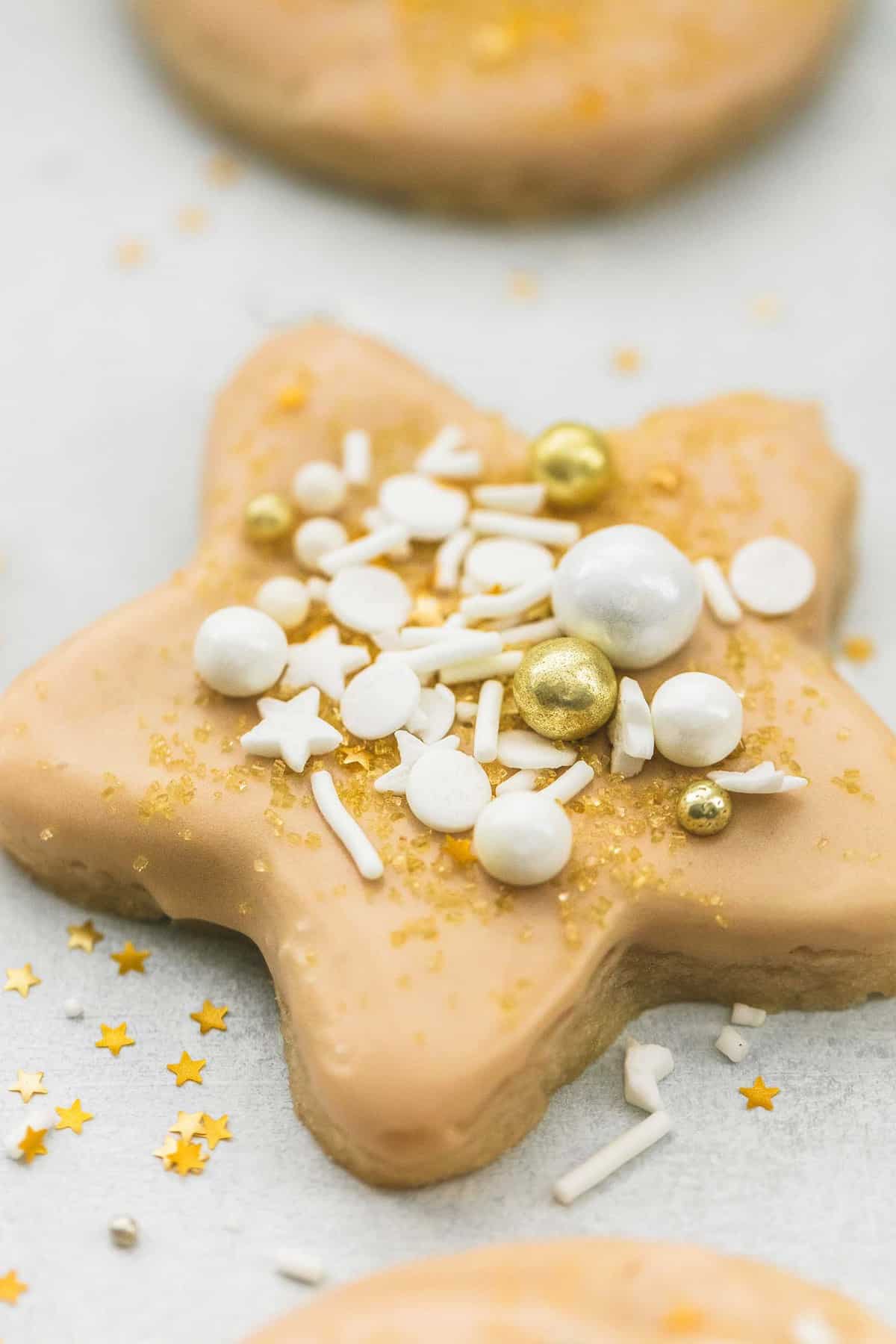 a maple glazed sugar cookie shaped as a star and topped with gold and white sprinkles.