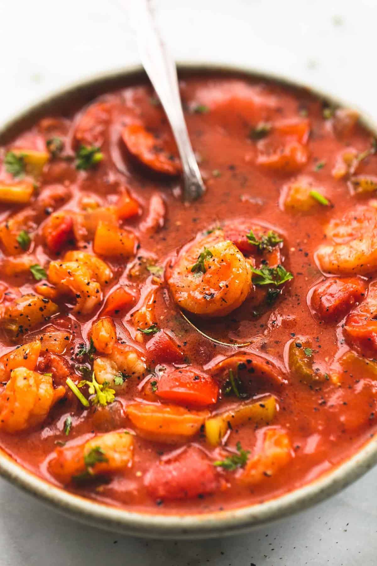 close up of shrimp and sausage gumbo with a spoon in a bowl.