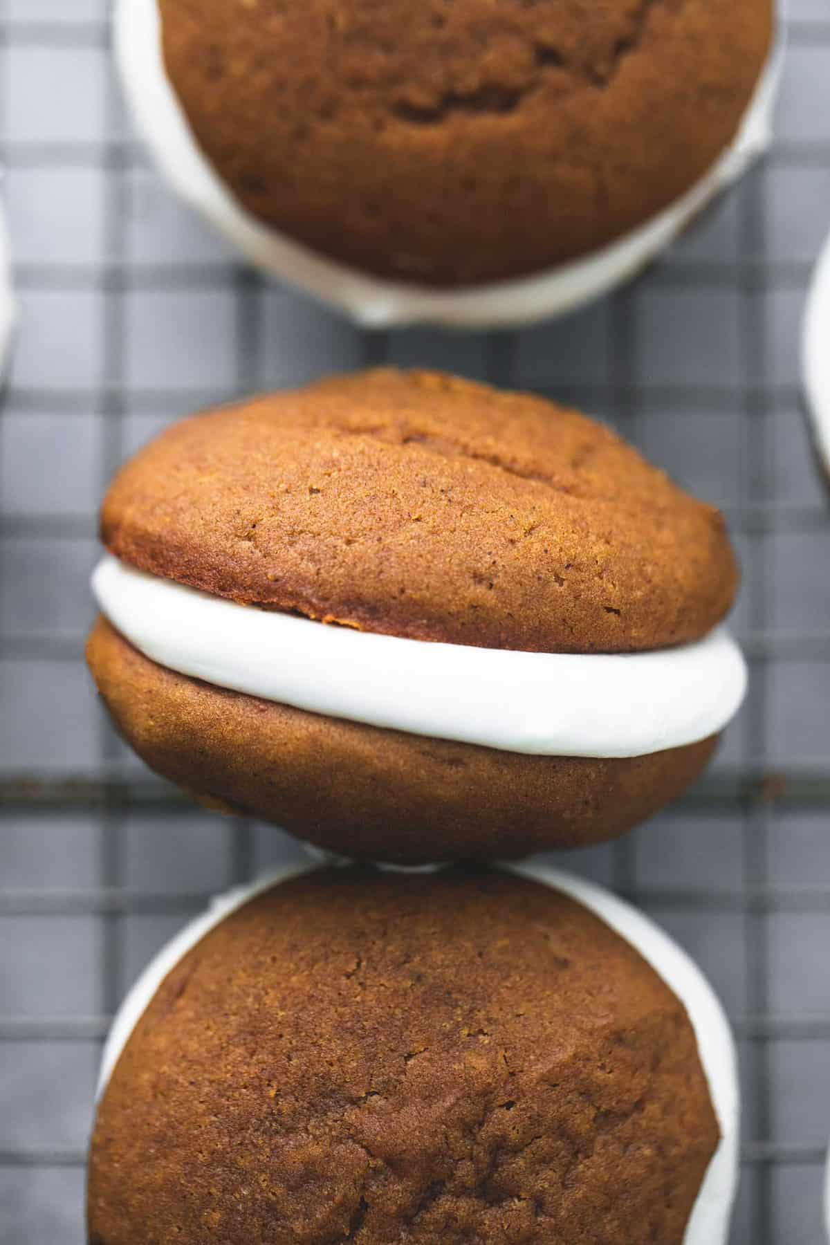 close up top view of gingerbread whoopie pies in a vertical row on a cooling rack with the middle one turned on it's side.