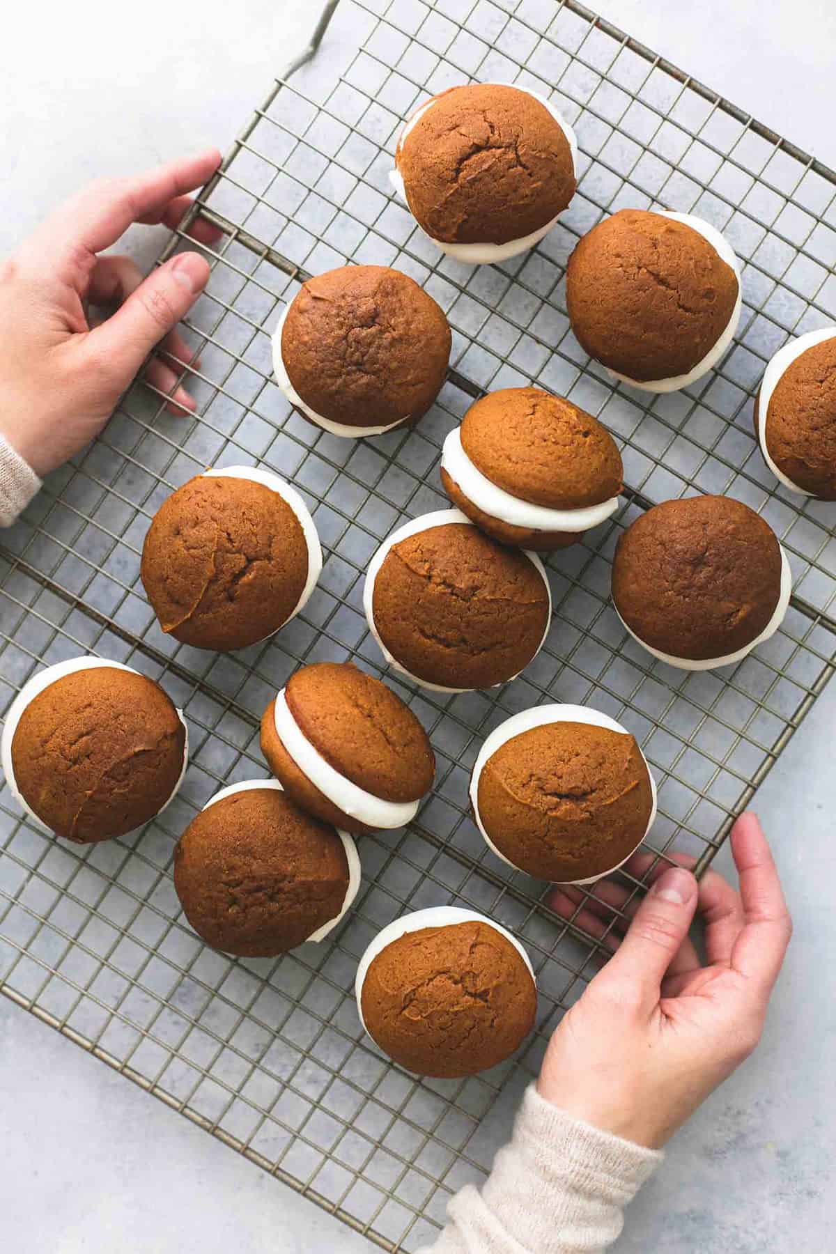 top view of a pair of hands holding a cooling rack of gingerbread whoopie pies.