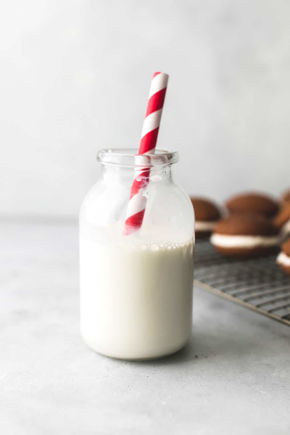 a jar of milk with a straw with gingerbread whoopie pies on a cooling rack in the background.