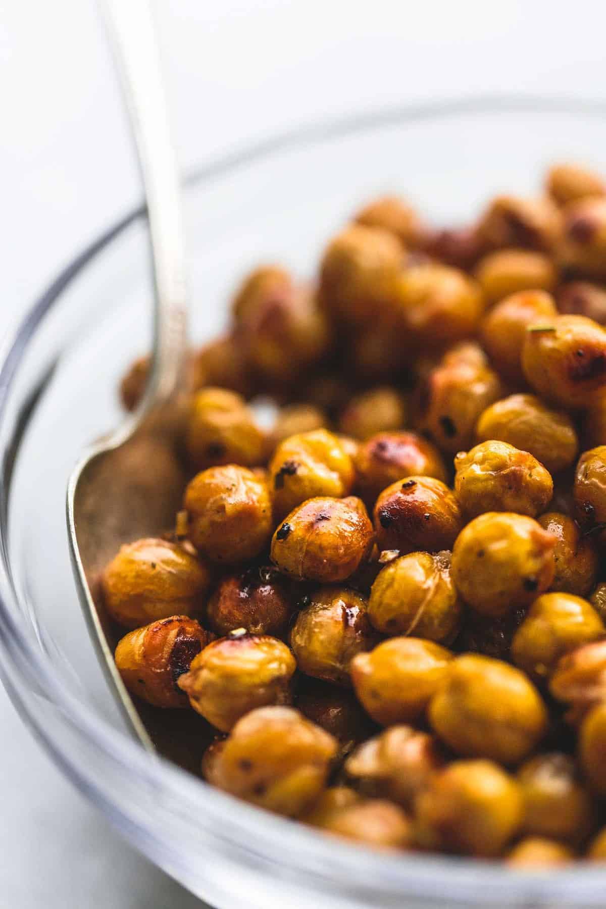 close up of chickpeas with a spoon in a glass bowl.