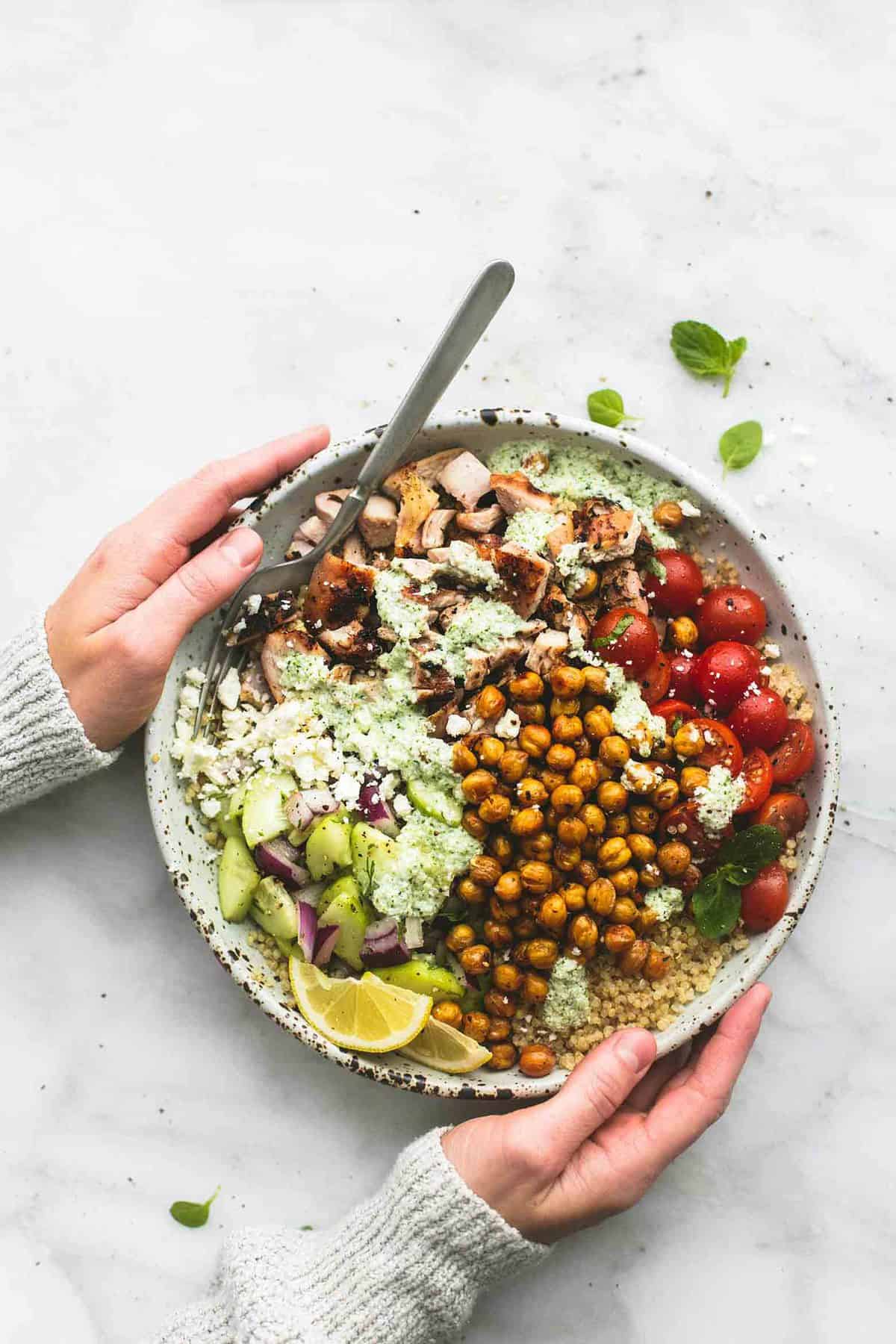 top view of hands holding a Greek chicken power bowl with a fork.